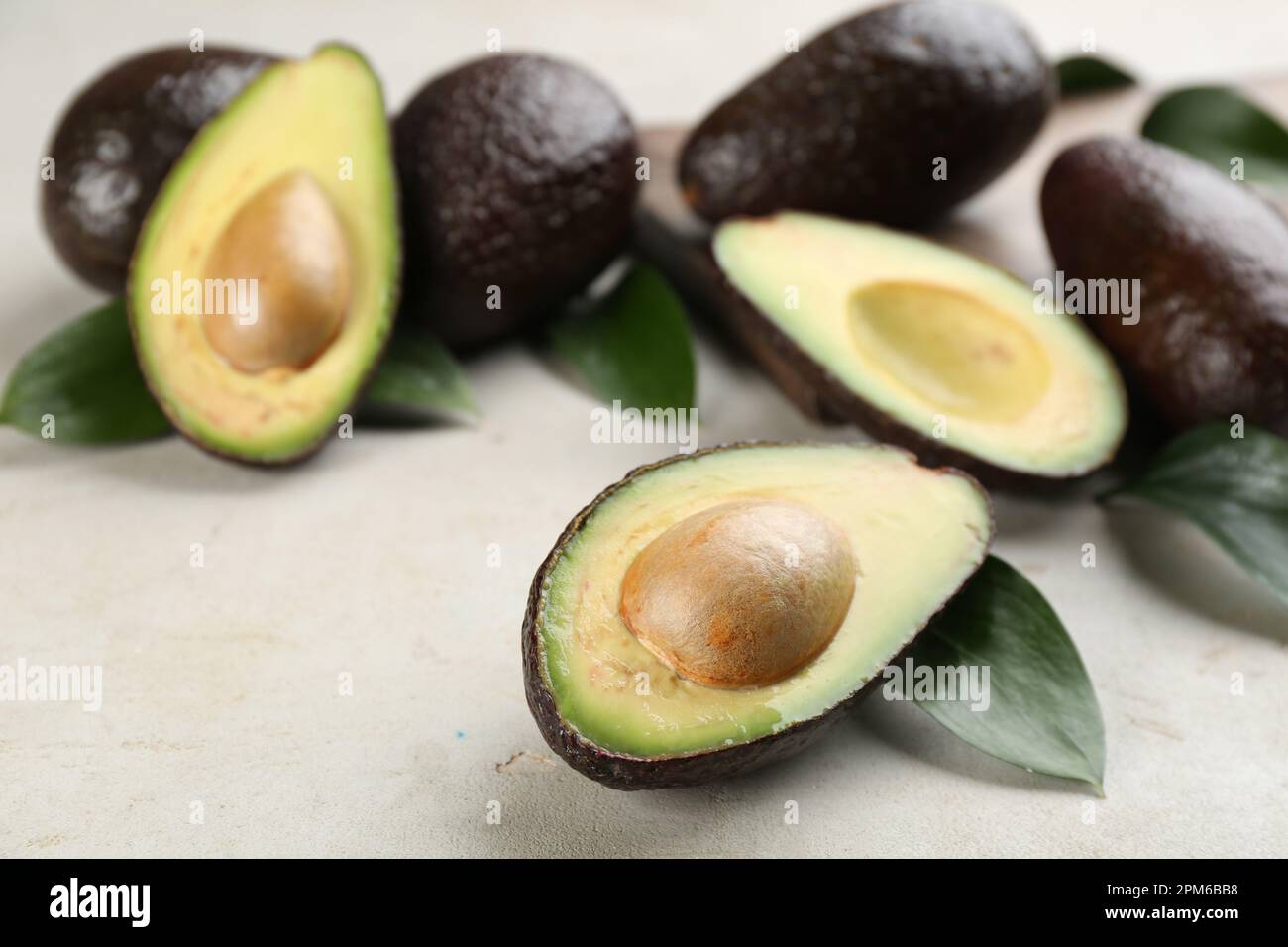Whole and cut avocados with green leaves on light table Stock Photo - Alamy