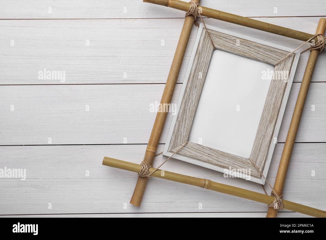 Empty bamboo frame on white wooden table, top view. Space for text ...
