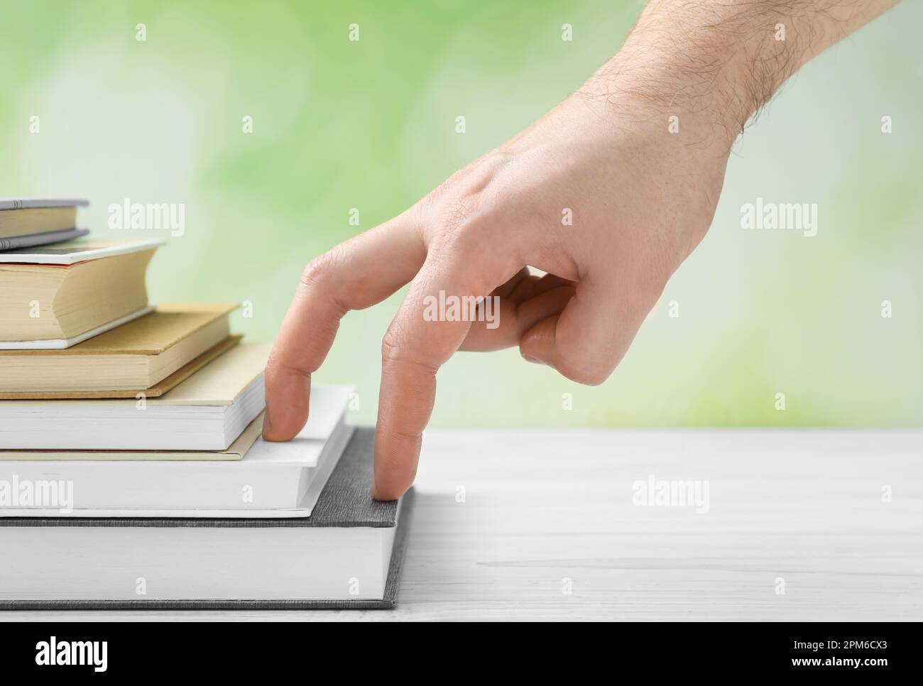 Man climbing up stairs of books with fingers on white wooden table against blurred background, closeup Stock Photo