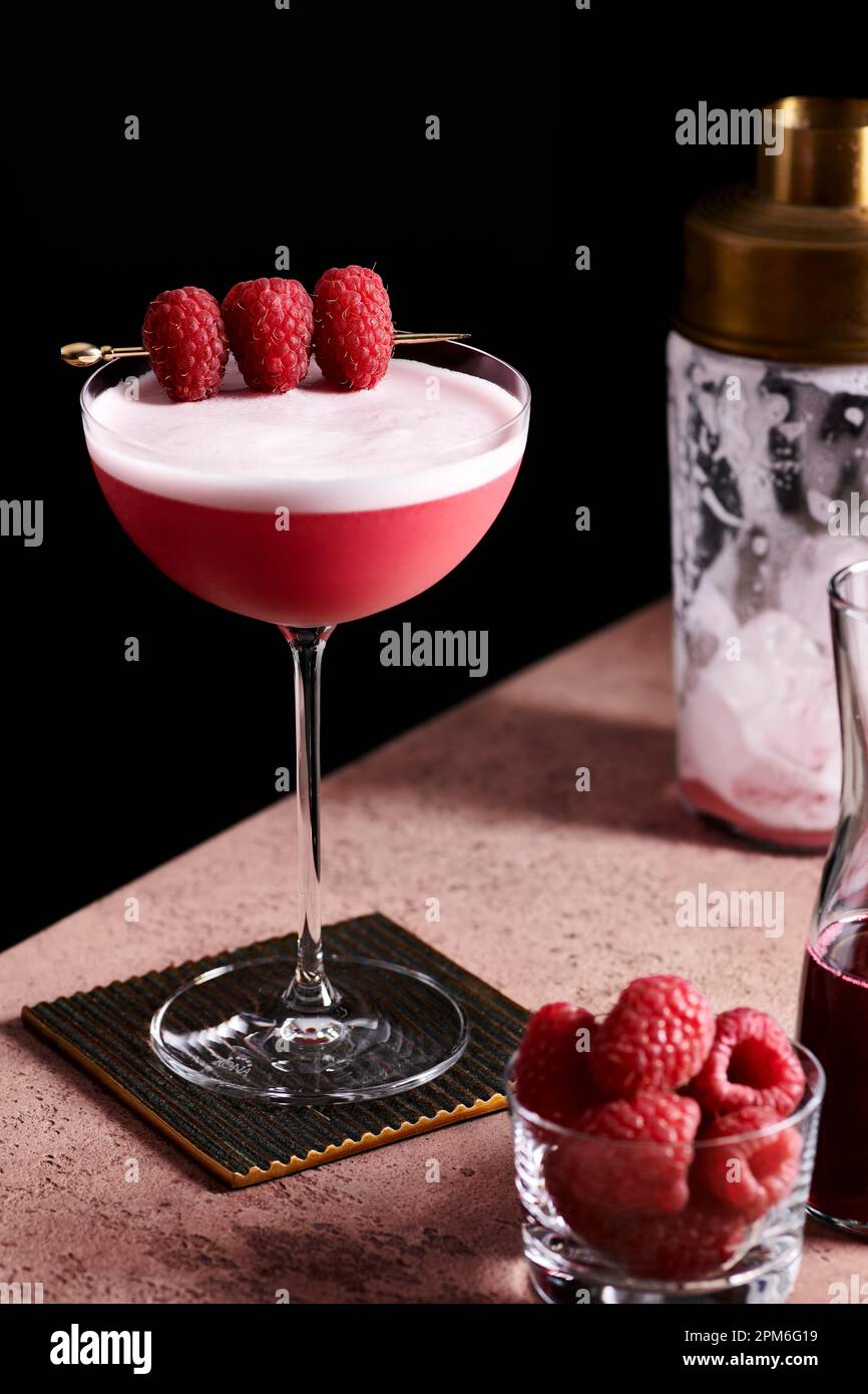 Clover club cocktail in a tall coupe glass garnished with three raspberries on a gold pick. Stock Photo