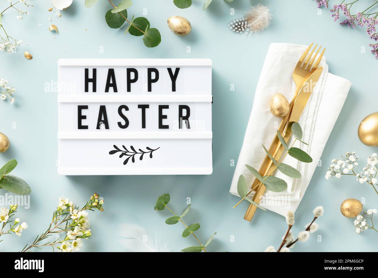 Easter table decorations. Stylish Easter brunch table setting with lightbox text Happy Easter, eggs, vintage cutlery, nests and spring branches on blu Stock Photo