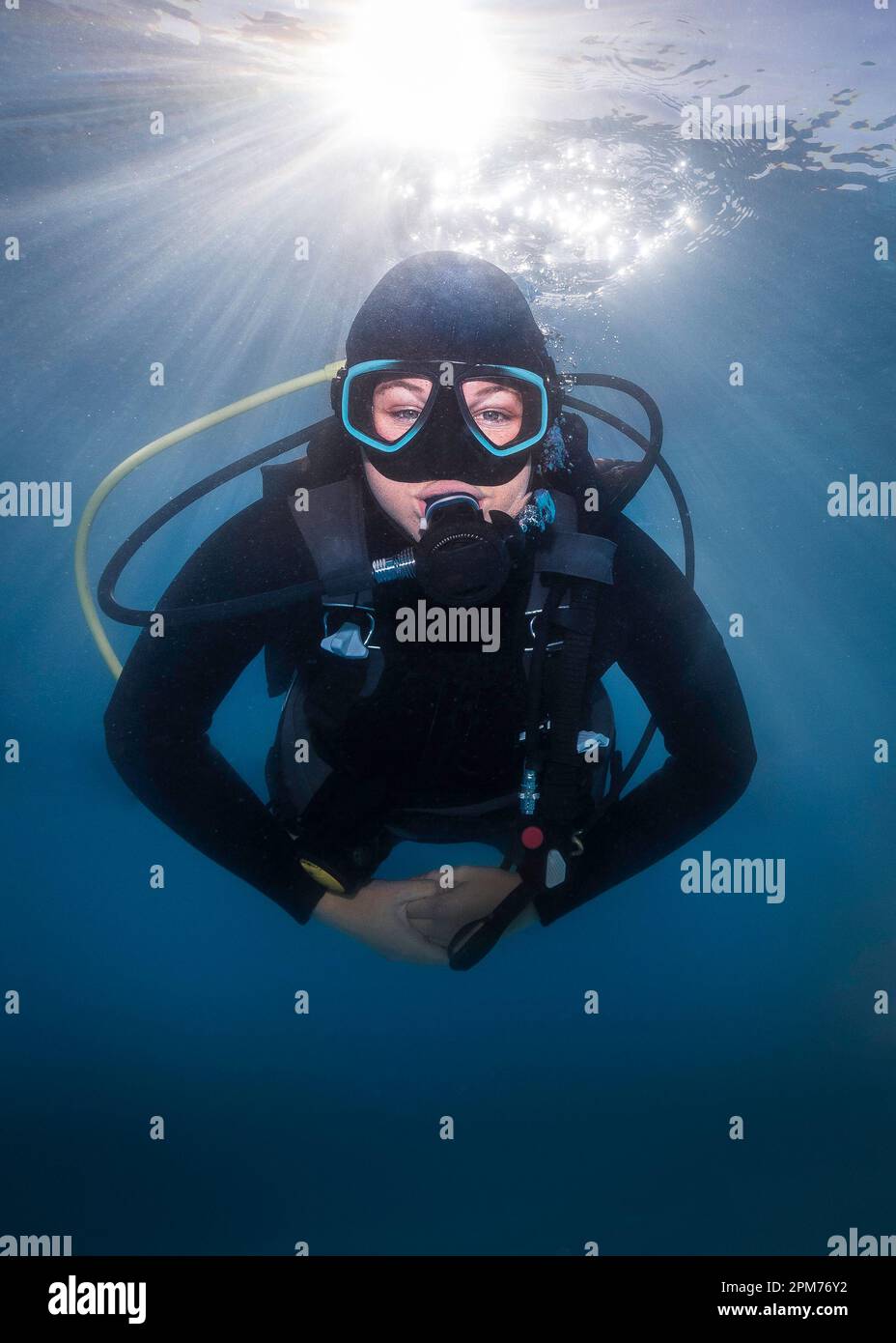 Closeup of a happy scuba diver underwater facing the camera with the bright sunrays shining through the water surface behind her Stock Photo