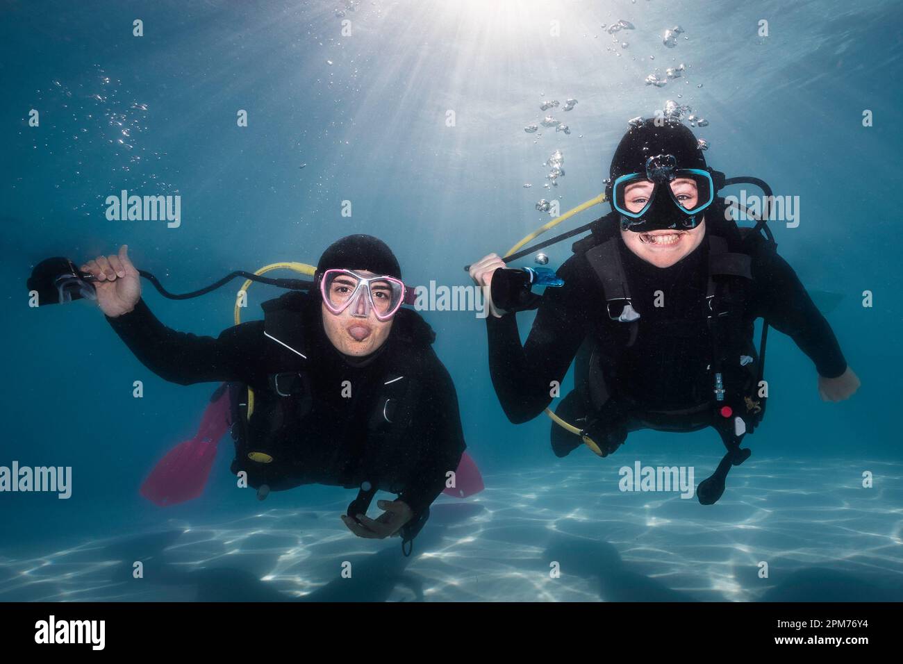 Closeup of two happy scuba divers holding their regulators in their hands underwater with one tongue out and smiling at the camera with the bright sun Stock Photo