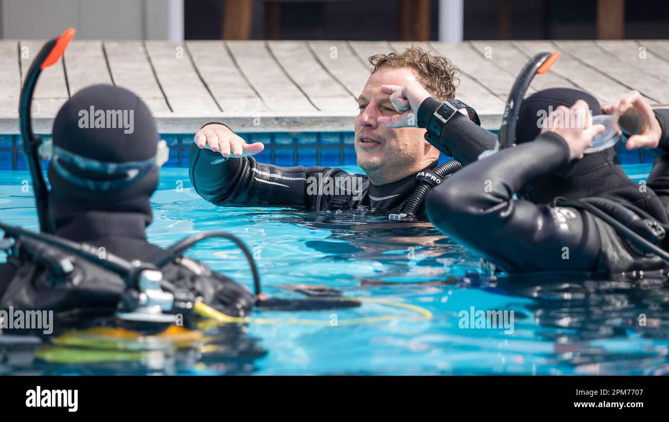 Scuba dive instructor teaching and explaining to students clearing your dive mask skills in the pool with his head tilted back Stock Photo