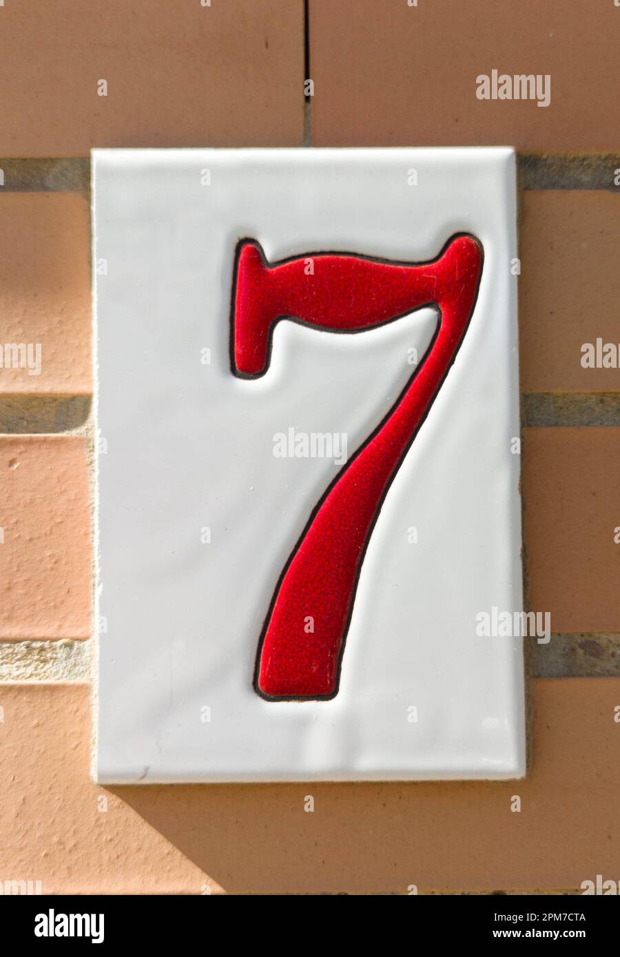House number 7 over brick sunny wall. Houses with personality concept. Stock Photo