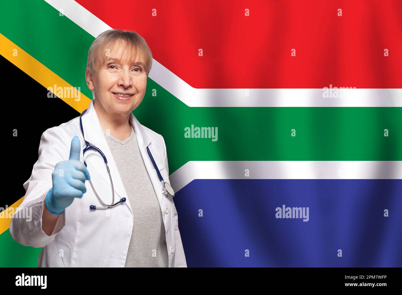South African smiling mature doctor woman holding stethoscope on flag