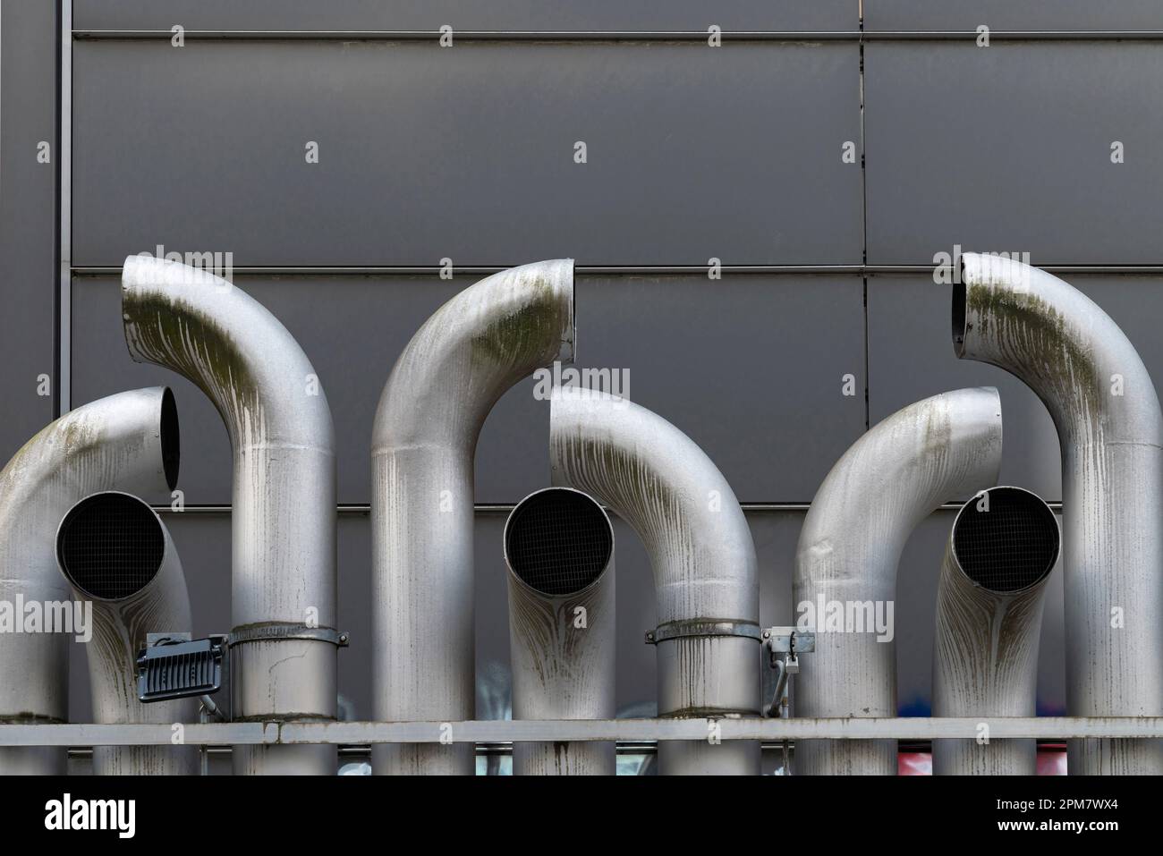 Curved metal exhaust pipes against a gray wall. Stock Photo