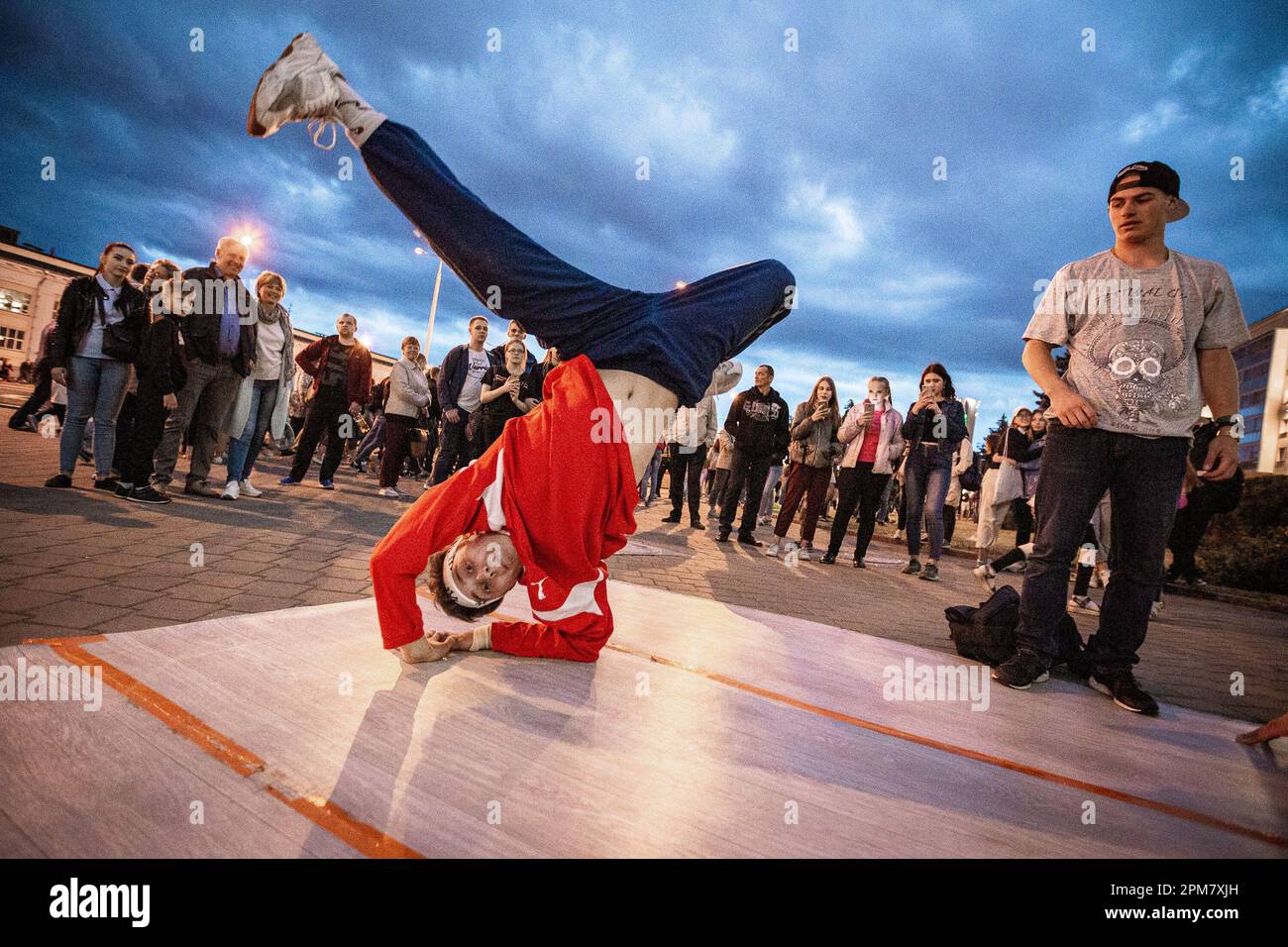 Minsk, Belarus. 3rd July, 2019. Konstantin and other b-boys start jamming. They quickly gather a curious audience and fill the street with hip-hop and funk music. 3rd July is the Independence Day of the Republic of Belarus. On this occasion each year, the authorities organize a military parade that follows Minsk's arteries. In this sublime time the city becomes a space of contrasts between dozens of soldiers and regular Belarusians, trying to live their normal lives. This cycle shows diversity of young Belarussian society.This project was shot in 2019 around the celebrations, and it meant to Stock Photo