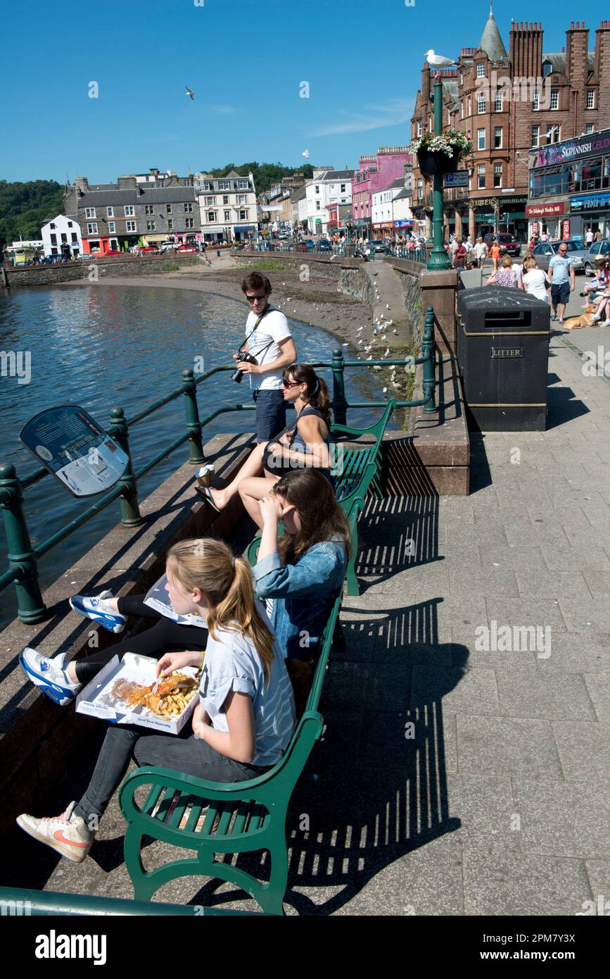 Girl on bench eating fish and chips on seafront, Oban, Argyll and Bute, Scotland, United Kingdom Stock Photo