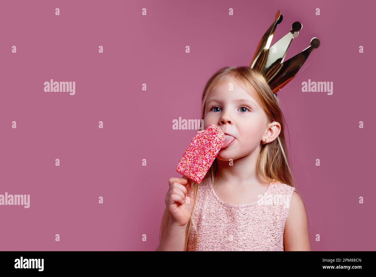 Cute little girl in a fancy dress and a crown eating ice-cream on pink ...