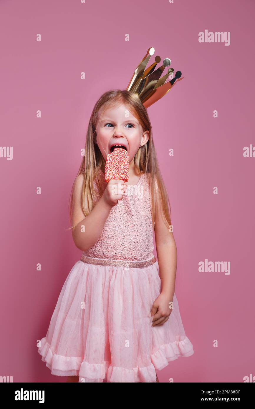 Cute little kid girl in pink dress and a crown eating ice-cream on pink ...