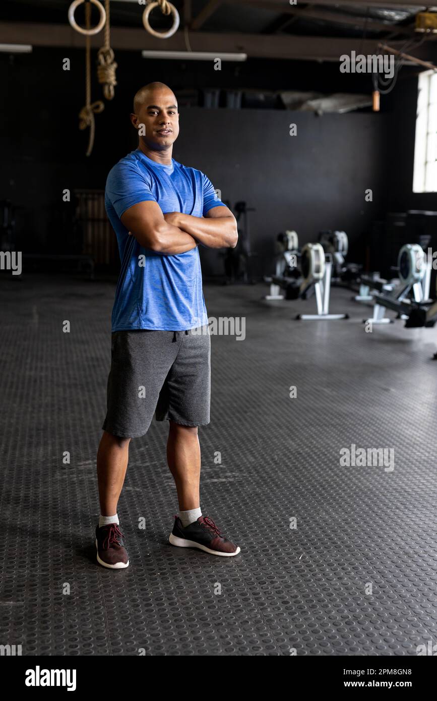 Full length of biracial confident young man with shaved head crossing arms and standing in gym Stock Photo