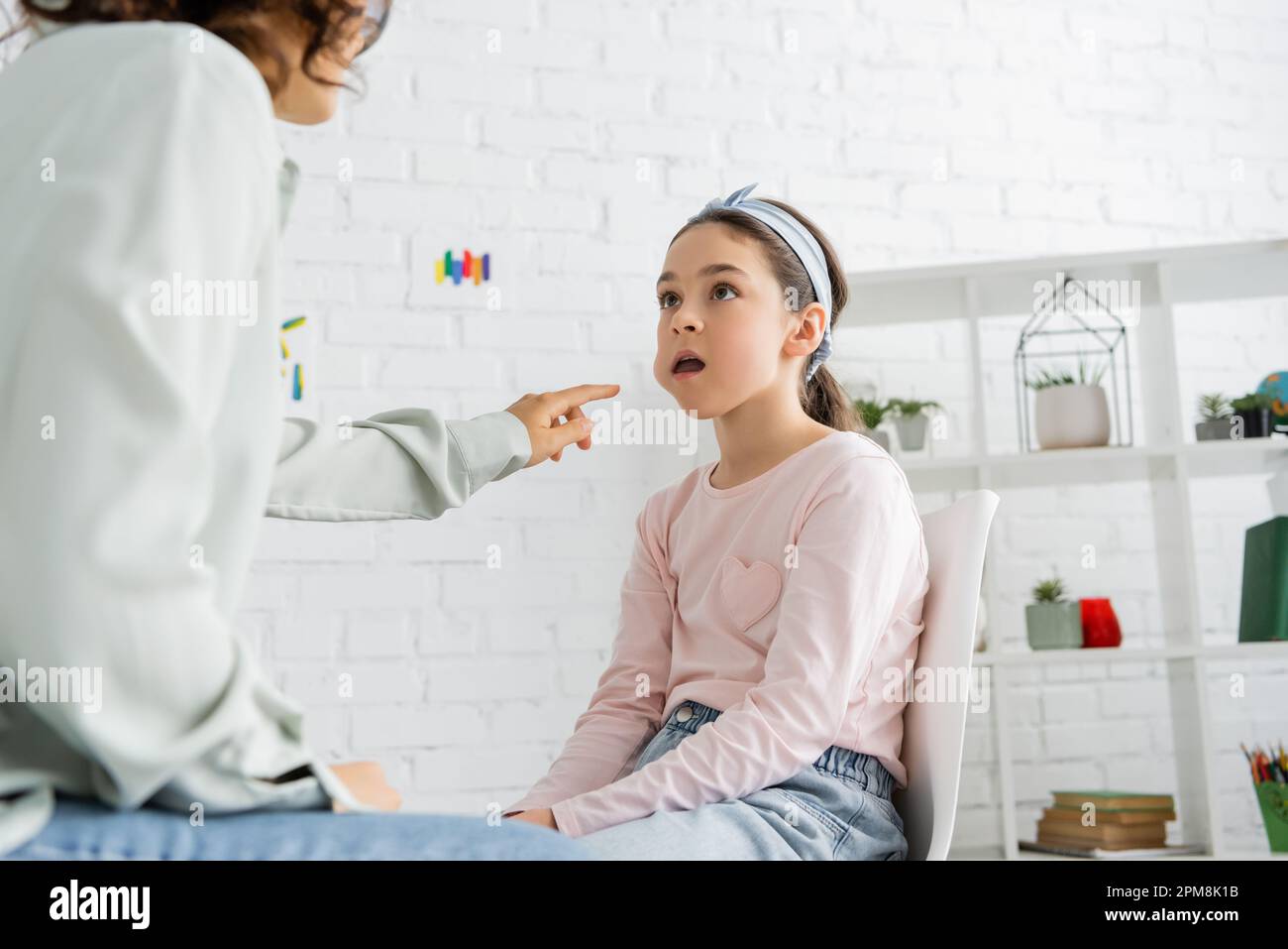 Speech therapist pointing at cheek of preteen girl in consulting room,stock image Stock Photo