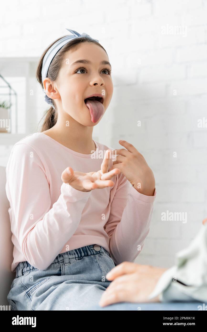Preteen pupil sticking out tongue during lesson with speech therapist,stock image Stock Photo