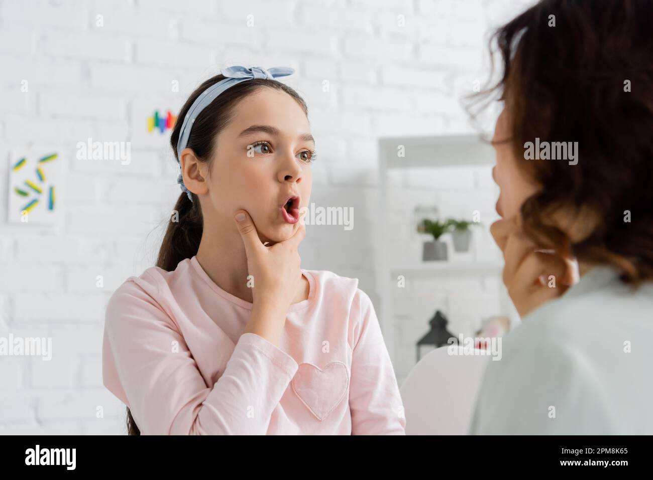 Preteen pupil touching cheeks and talking during lesson with speech therapist,stock image Stock Photo