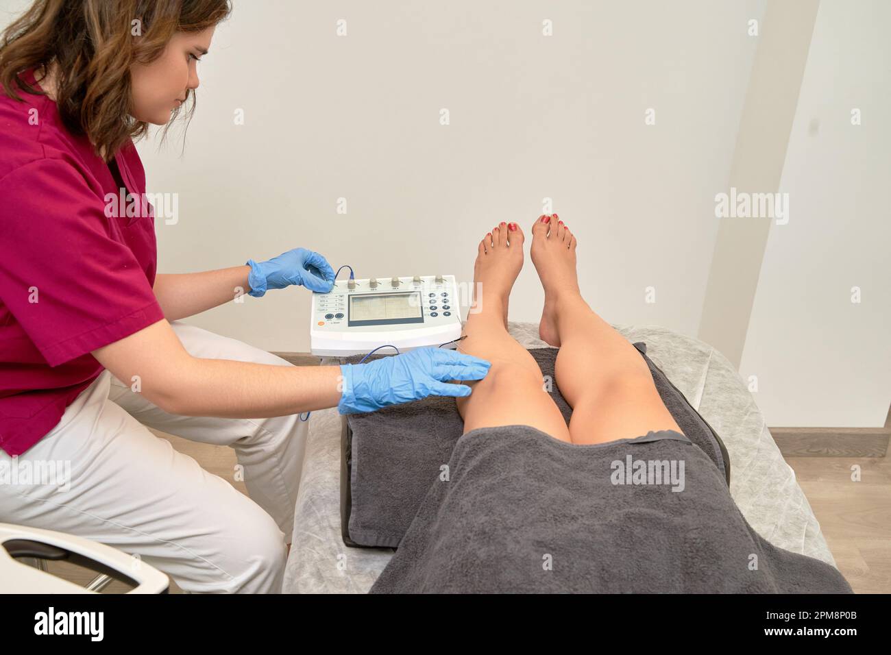 A physical therapist performs percutaneous electrolysis treatment on a patient's leg using advanced electrotherapy equipment and techniques to relieve pain. Stock Photo