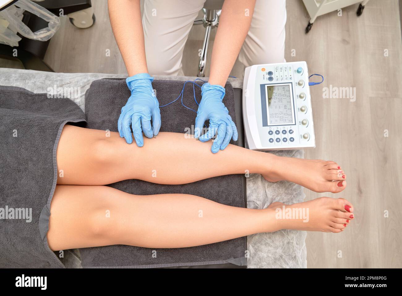 An experienced physiotherapist administers safe and effective percutaneous electrolysis therapy to a patient's leg using modern electrotherapy equipment.  Stock Photo