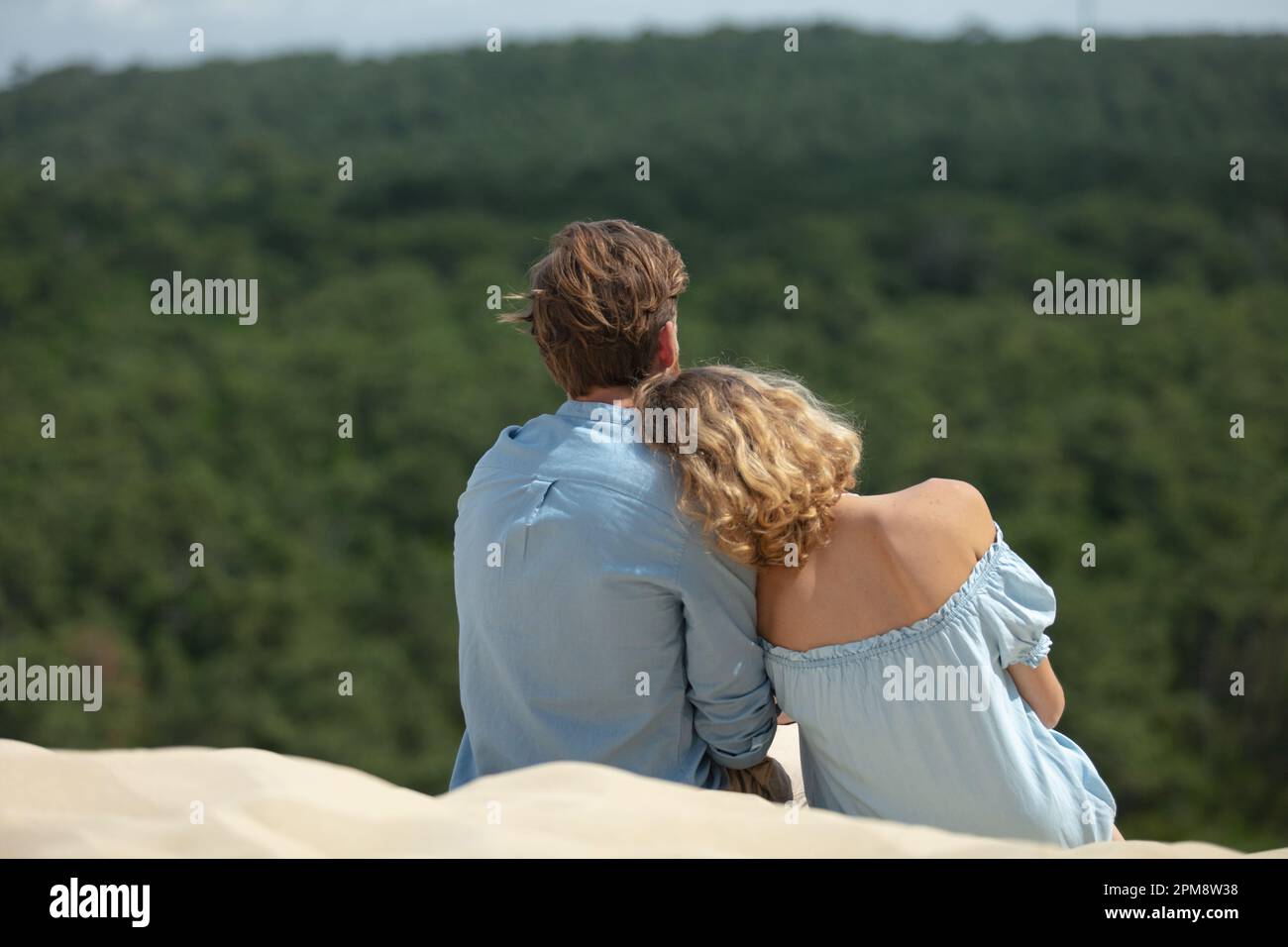 couple sitting and hugging on dune in front of forest Stock Photo