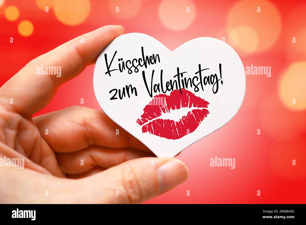 FOTOMONTAGE, Hand hält weißes Herz mit Lippenabdruck und Aufschrift Küsschen zum Valentinstag Stock Photo