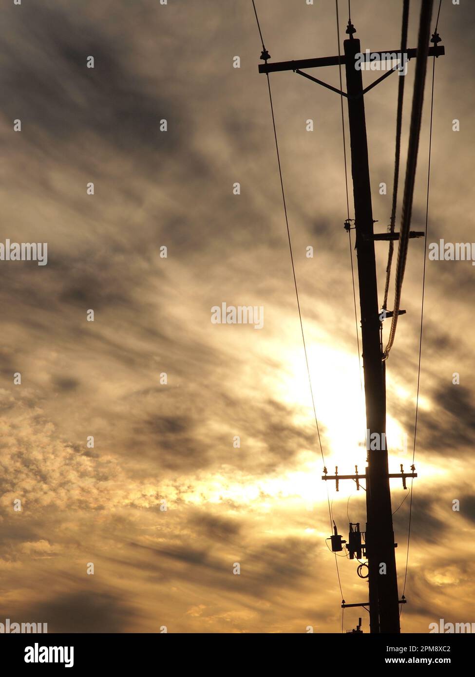 Silhouetted utility pole with cloudy sunset behind. Stock Photo