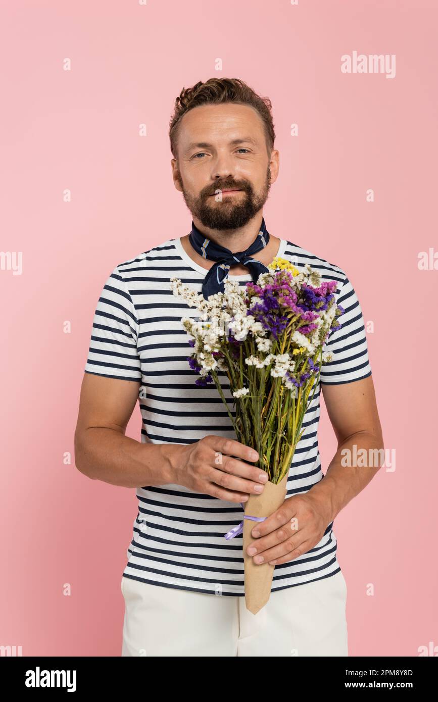 happy man in striped t-shirt and neck scarf holding flowers in paper wrap isolated on pink,stock image Stock Photo