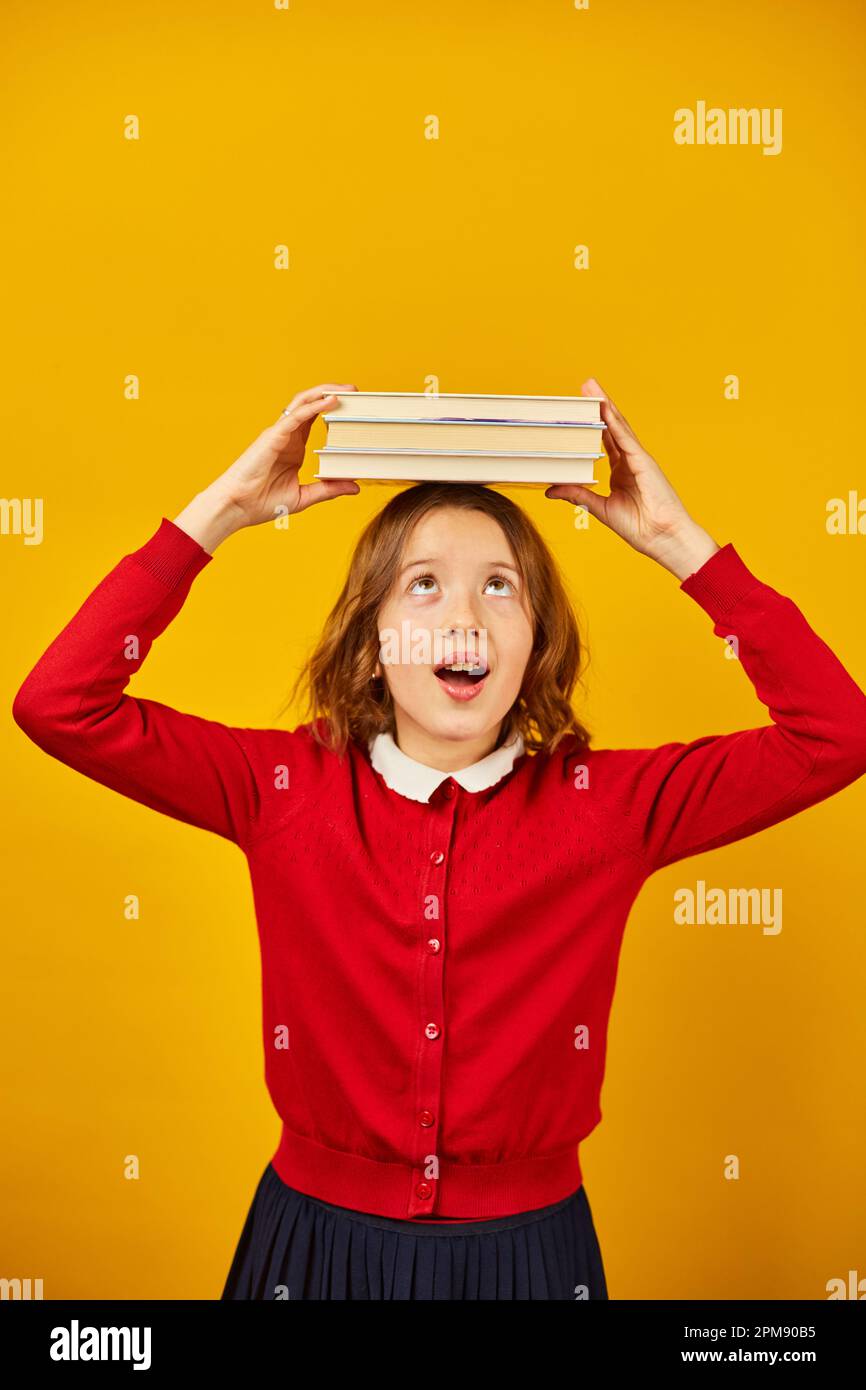 Portrait of happy teenage schoolgirl in uniform holding books on head ...