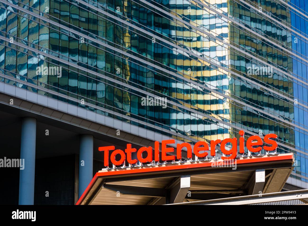 Sign of a TotalEnergies service station with a glass building in the background. Stock Photo