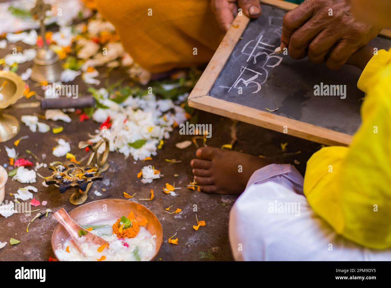 Aksharabhyasam or hate khori ritual is being performed to introduce education to young children during Saraswati Puja or vasant panchami. The priest i Stock Photo