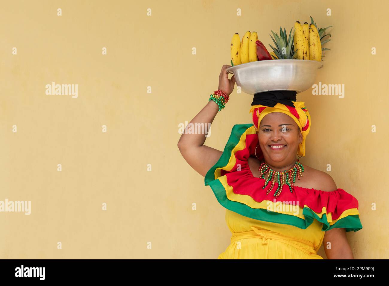 Happy smiling Palenquera fresh fruit street vendor in the Historic District of Cartagena, Colombia. Cheerful Colombian woman in traditional costumes. Stock Photo