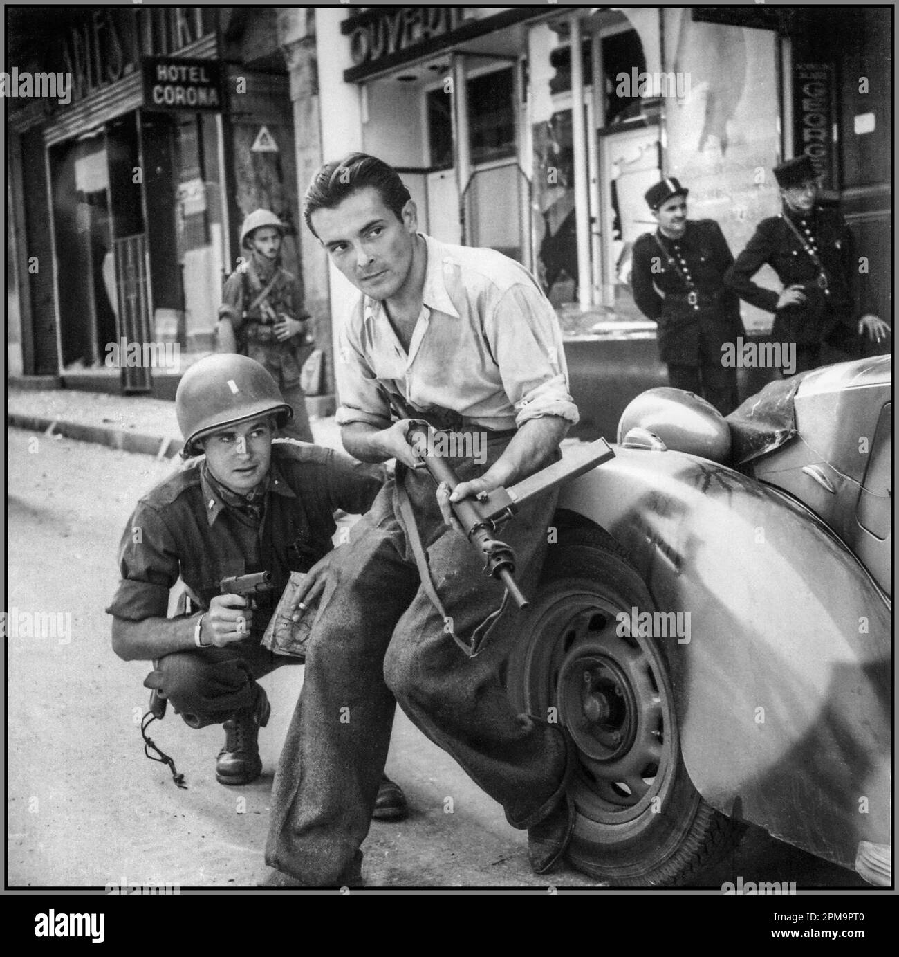 FRENCH RESISTANCE PARTISAN 1944 American Lieutenant Edwin E. Dowell with a Colt pistol and a French partisan with an English-made submachine gun during a street battle in Marseille. France. Noteworthy are the police officers in the background and the camouflage coloring of the car. Marseille France.The French Resistance (French: La Résistance) was a collection of groups that fought the Nazi occupation of France and the collaborationist Vichy régime in France during the Second World War. Resistance cells were small groups of armed men and women called the Maquis in rural France Stock Photo