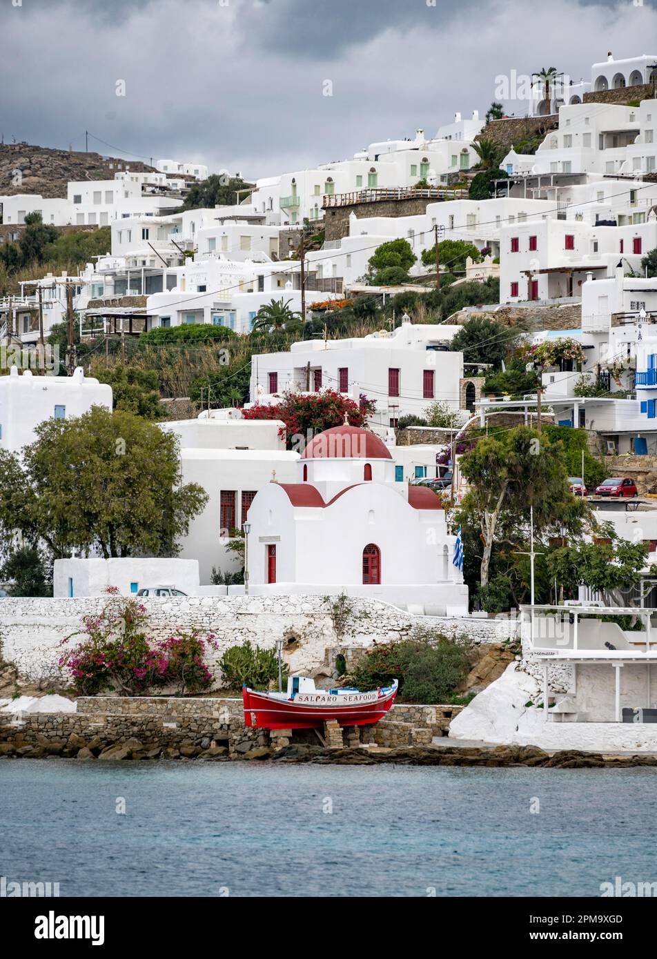 Fishing boat and small Greek Orthodox white church with red roof, Holy Church of Rodon and Amaranto, Old Port of Mykonos, Chora, Mykonos Town Stock Photo