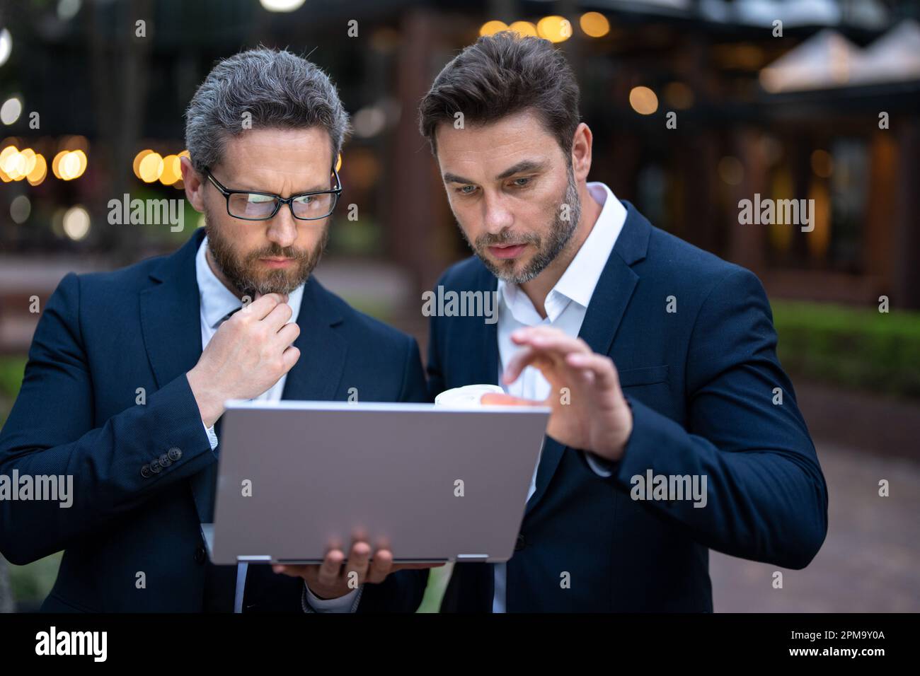 Business men team using laptop outdoor. Businessmen looking laptop with their business success in city background. Two business teams success Stock Photo