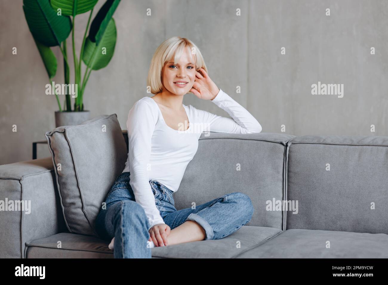 Beautiful blonde girl is sitting on the couch and looking at the camera ...
