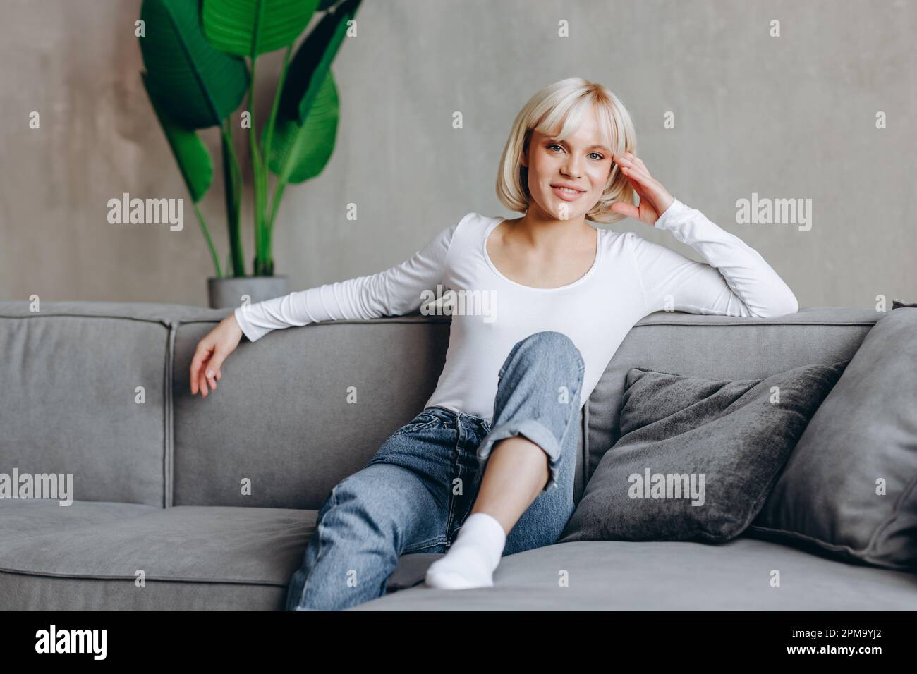 Beautiful blonde girl is sitting on the couch and looking at the camera ...