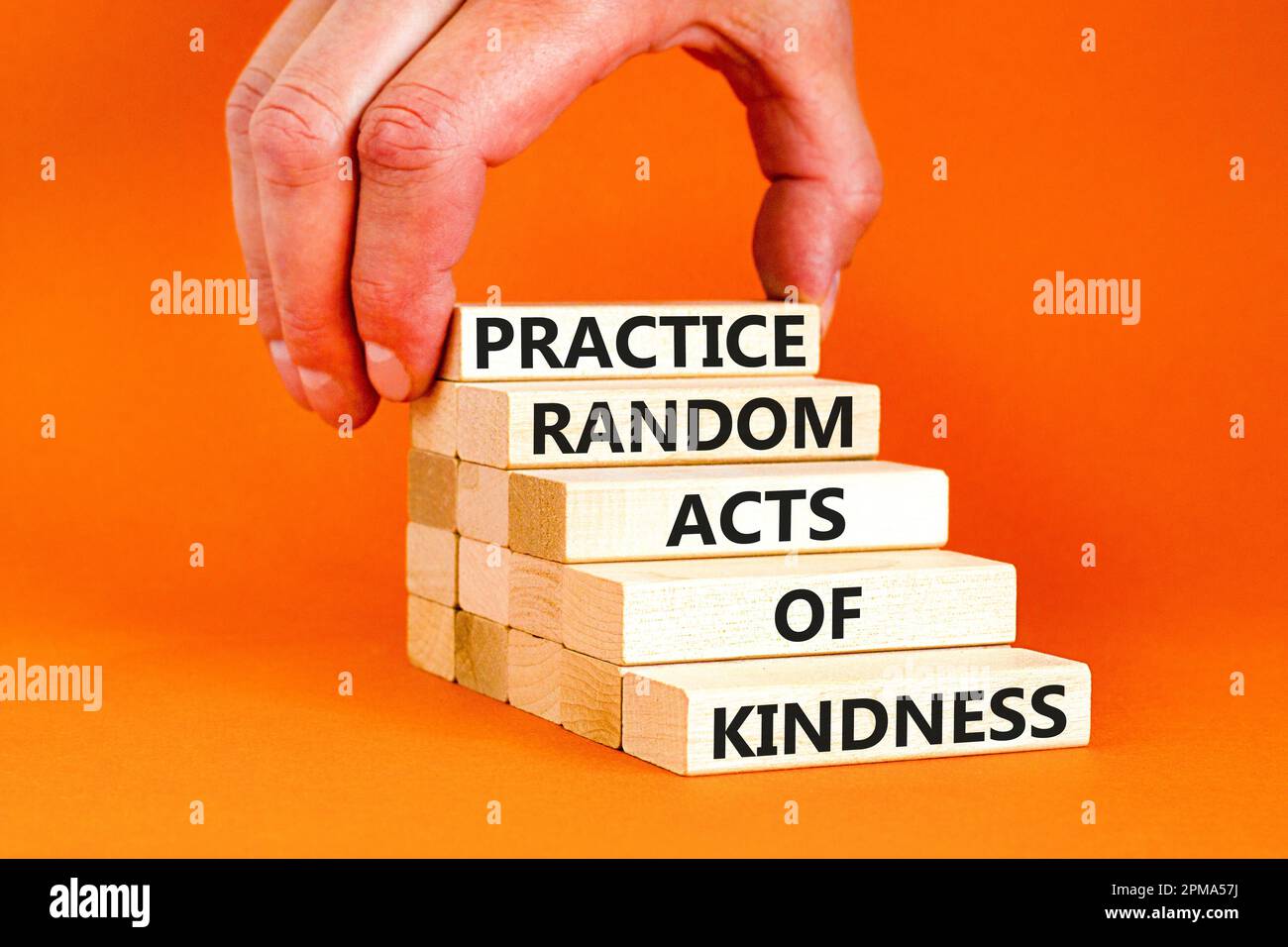 Practice random kind of kindness symbol. Concept words Practice random kind of kindness on wooden block. Beautiful orange background. Businessman hand Stock Photo
