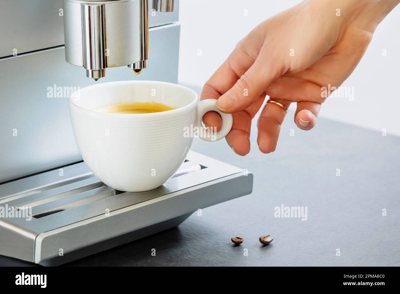 Female hand taking of cup of fresh hot espresso pouring from coffee machine. Professional coffee brewing. Cup of natural espresso. Coffee break. Good Stock Photo