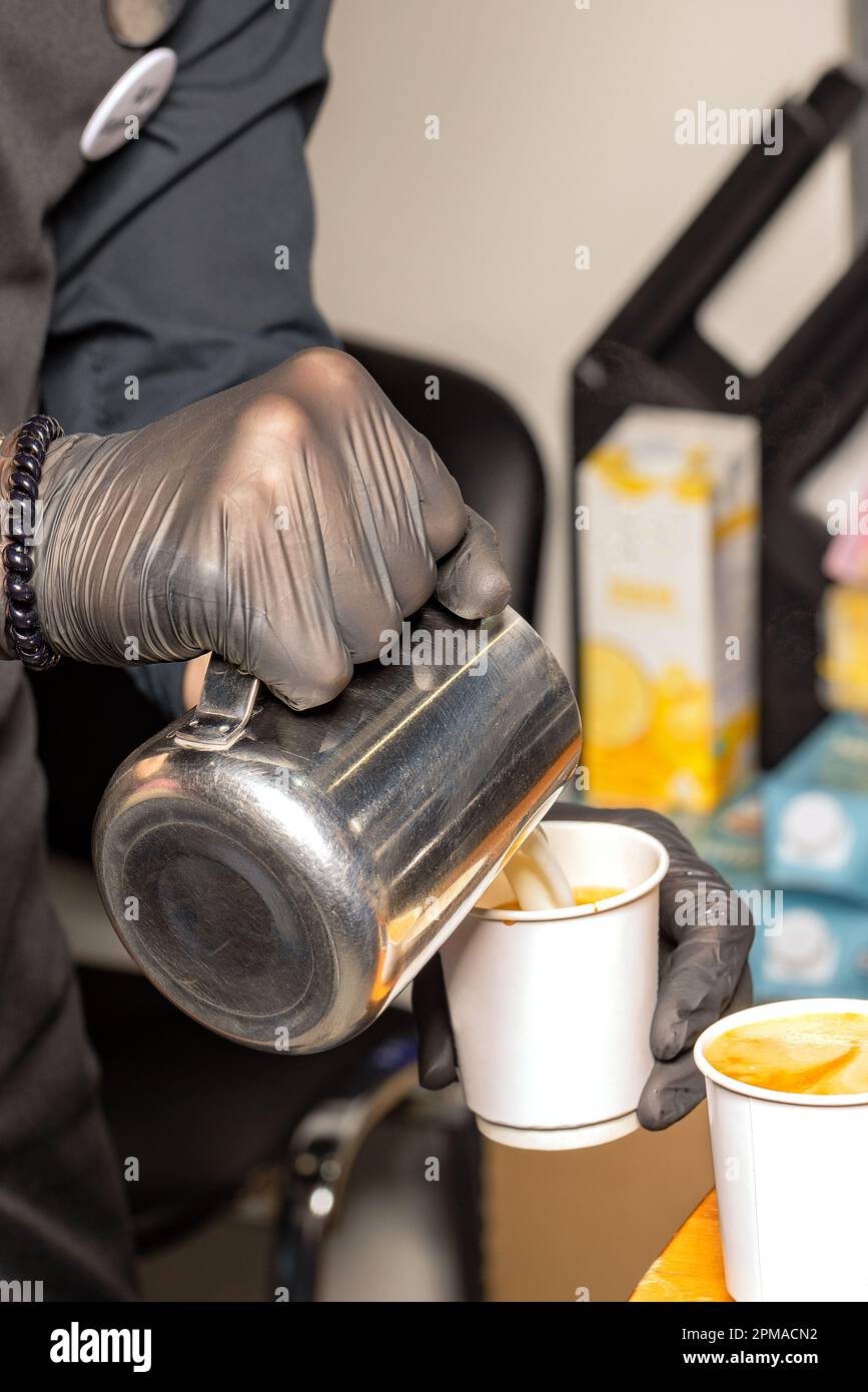A professional barista pours steamed milk into a coffee paper cup while ...