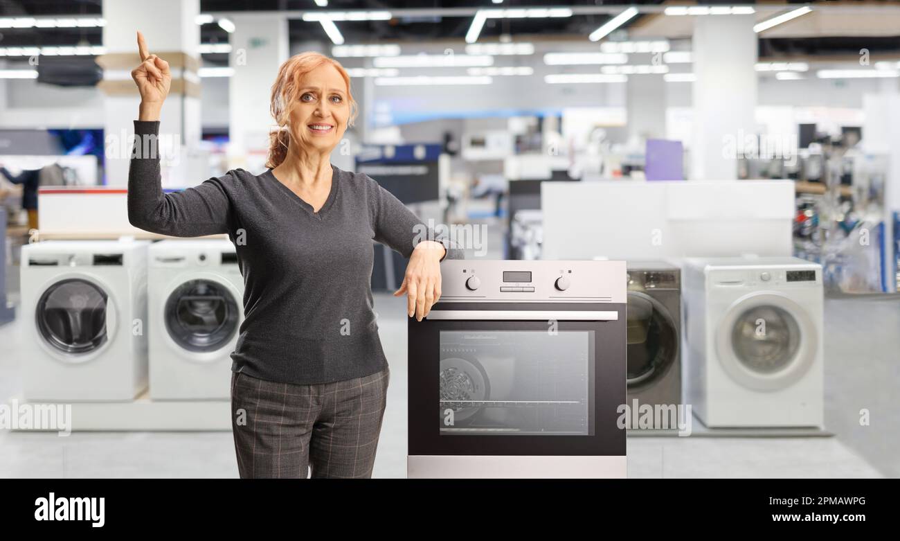Happy mature woman pointing up and leaning on an oven inside a home applances store Stock Photo