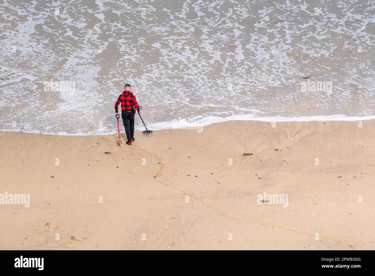 A metal detectorist searching on the shoreline at Tolcarne Beach in