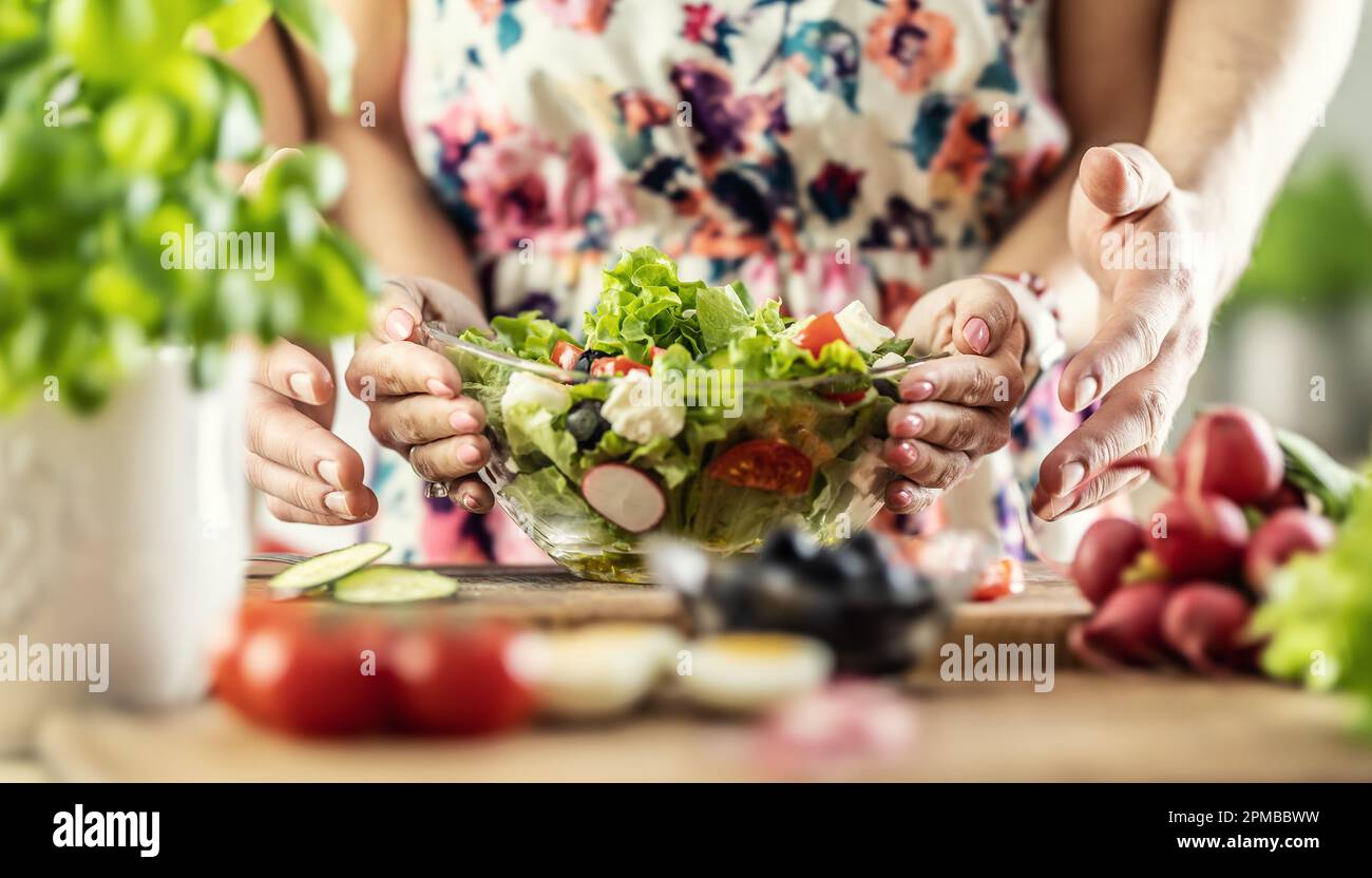 A man and a woman prepared a healthy spring salad. Together they hold a bowl of healthy food with their hands. Stock Photo