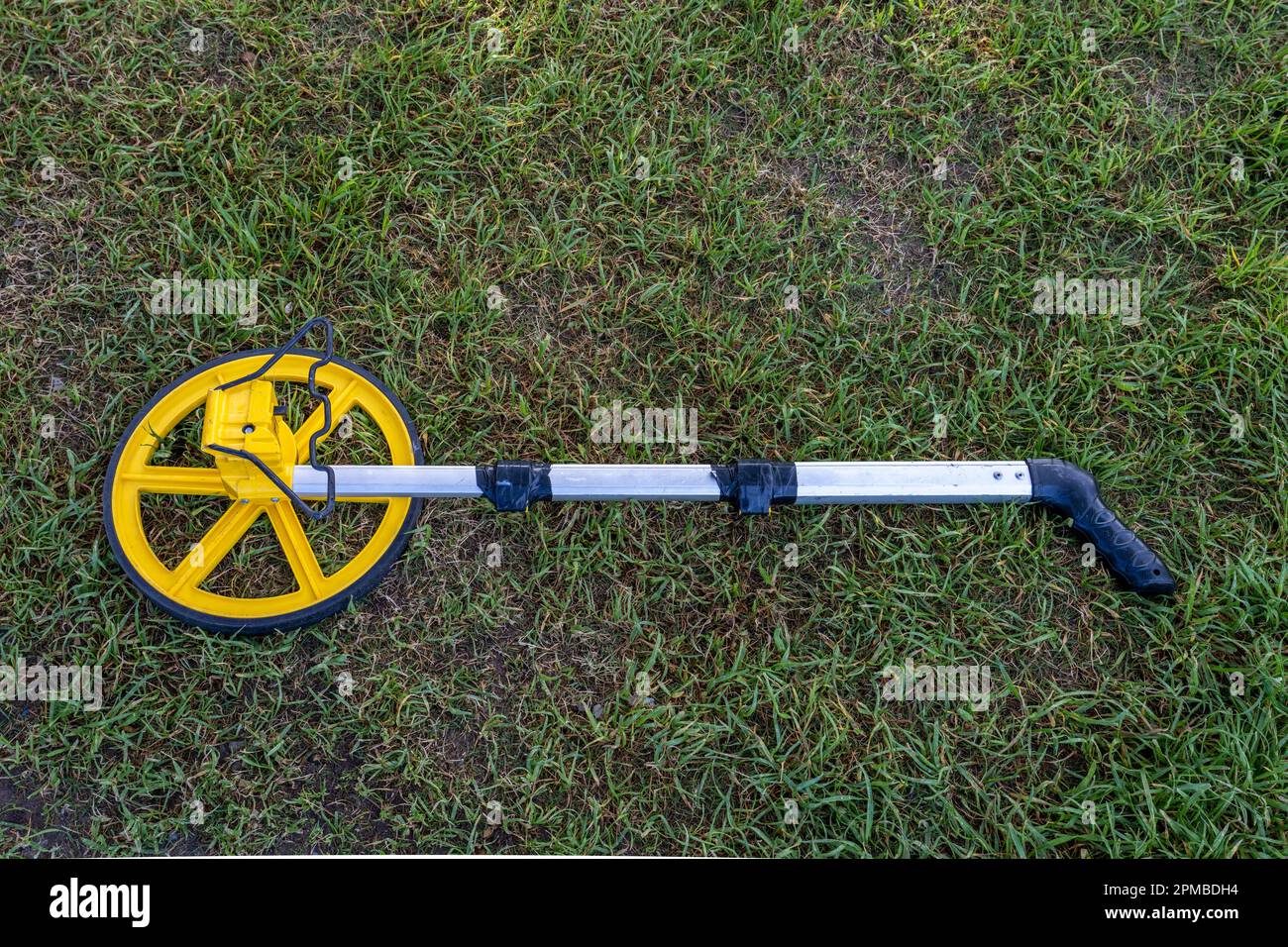 Measuring wheel device with telescoping handle taped to size, laying on the grass Stock Photo