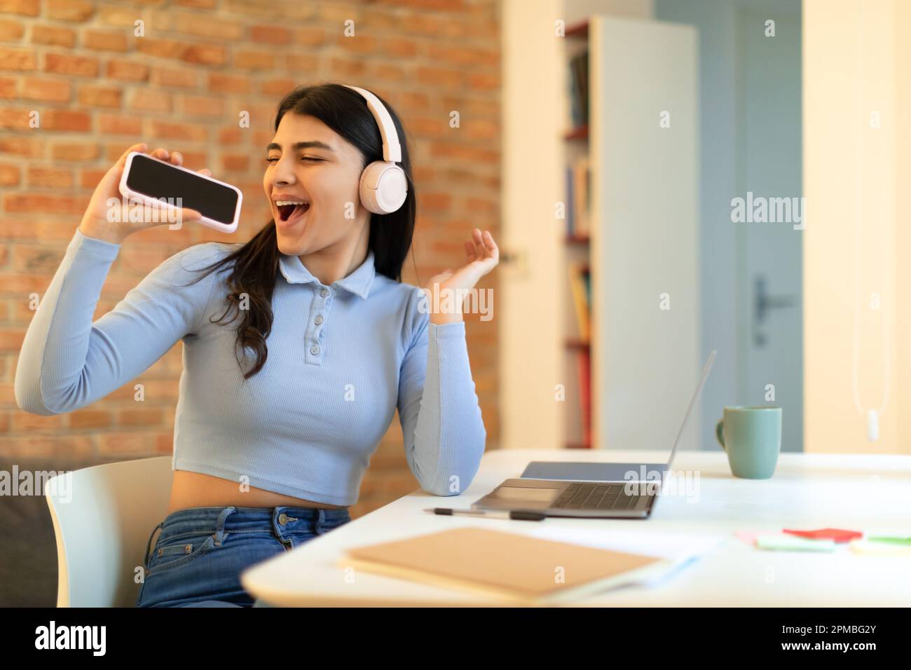 Joyful spanish lady in wireless headphones singing in cellphone as mic