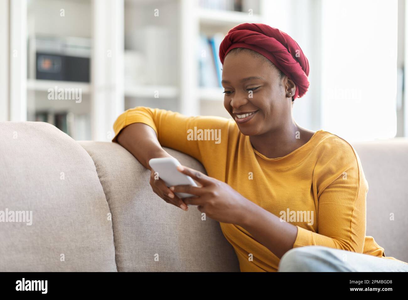 Happy african american woman sitting on couch, using smartphone Stock ...