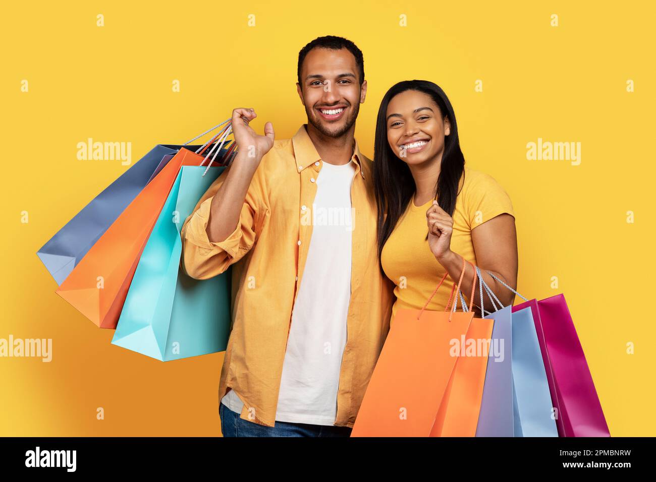 Cheerful millennial african american guy and woman hold many bags of ...