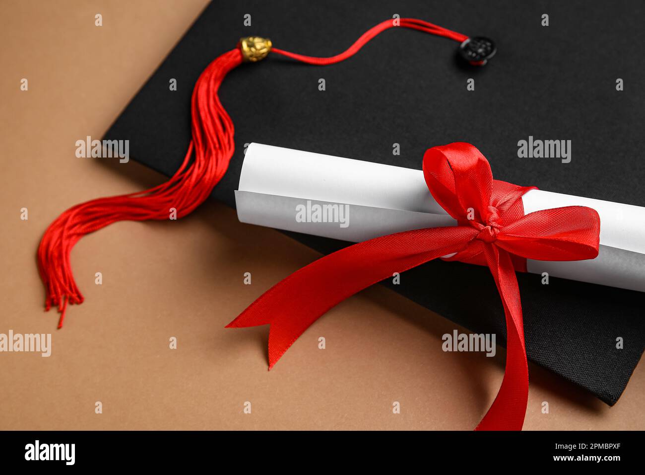 Diploma with red ribbon and graduation hat on brown background Stock ...