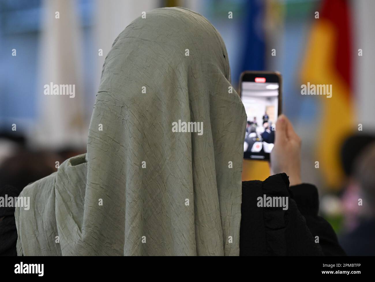 Mainz, Germany. 12th Apr, 2023. A woman wearing the hijab takes a photo during a speech before breaking the fast in the banquet hall of the Islamic Community of Bosniaks (IGDB). During the fasting month of Ramadan, the Muslim communities in Rhineland-Palatinate also invite non-Muslims to break their fast (iftar) in the evening. Credit: Arne Dedert/dpa/Alamy Live News Stock Photo