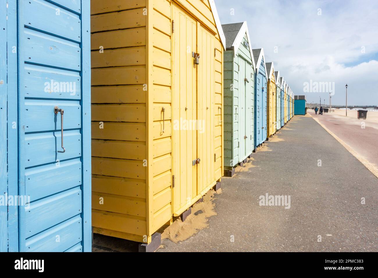 A path in front of beach huts on Bournemouth Beach in Dorset, UK under a stormy, grey sky with sand blowing in the wind Stock Photo