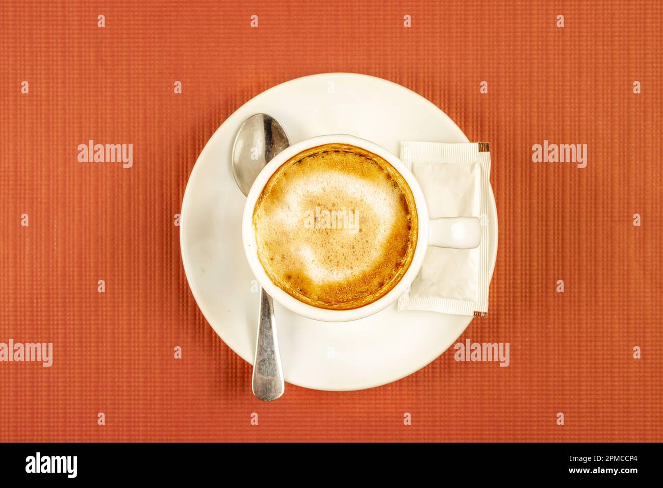 A latte served in a bar cup with a sugar packet and a teaspoon Stock
