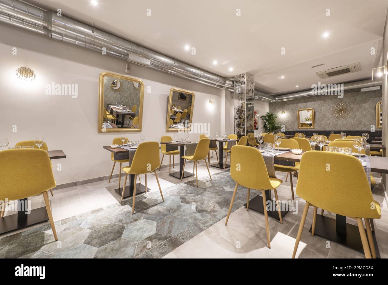 Dining room of a restaurant with assembled tables and chairs upholstered in yellow fabric and exposed air conditioning pipes Stock Photo