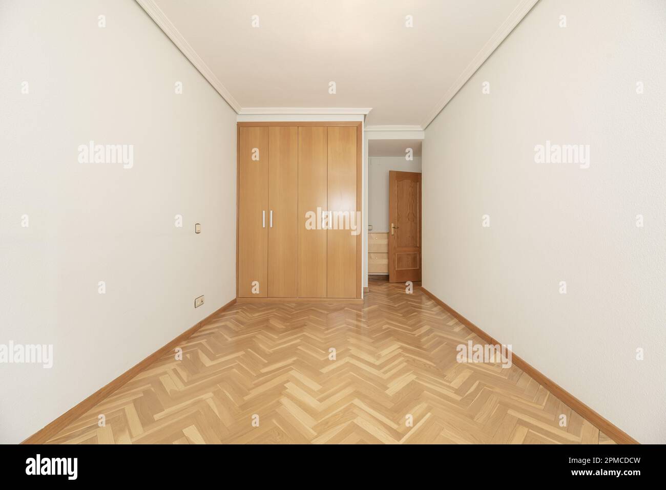 Empty room with built-in wardrobe with four oak folding doors and glossy varnished wooden floors and matching access door Stock Photo